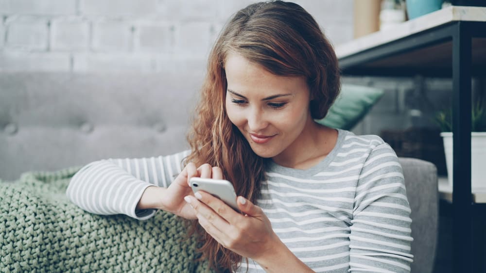 Une femme assise sur un canapé écrit un message sur son téléphone