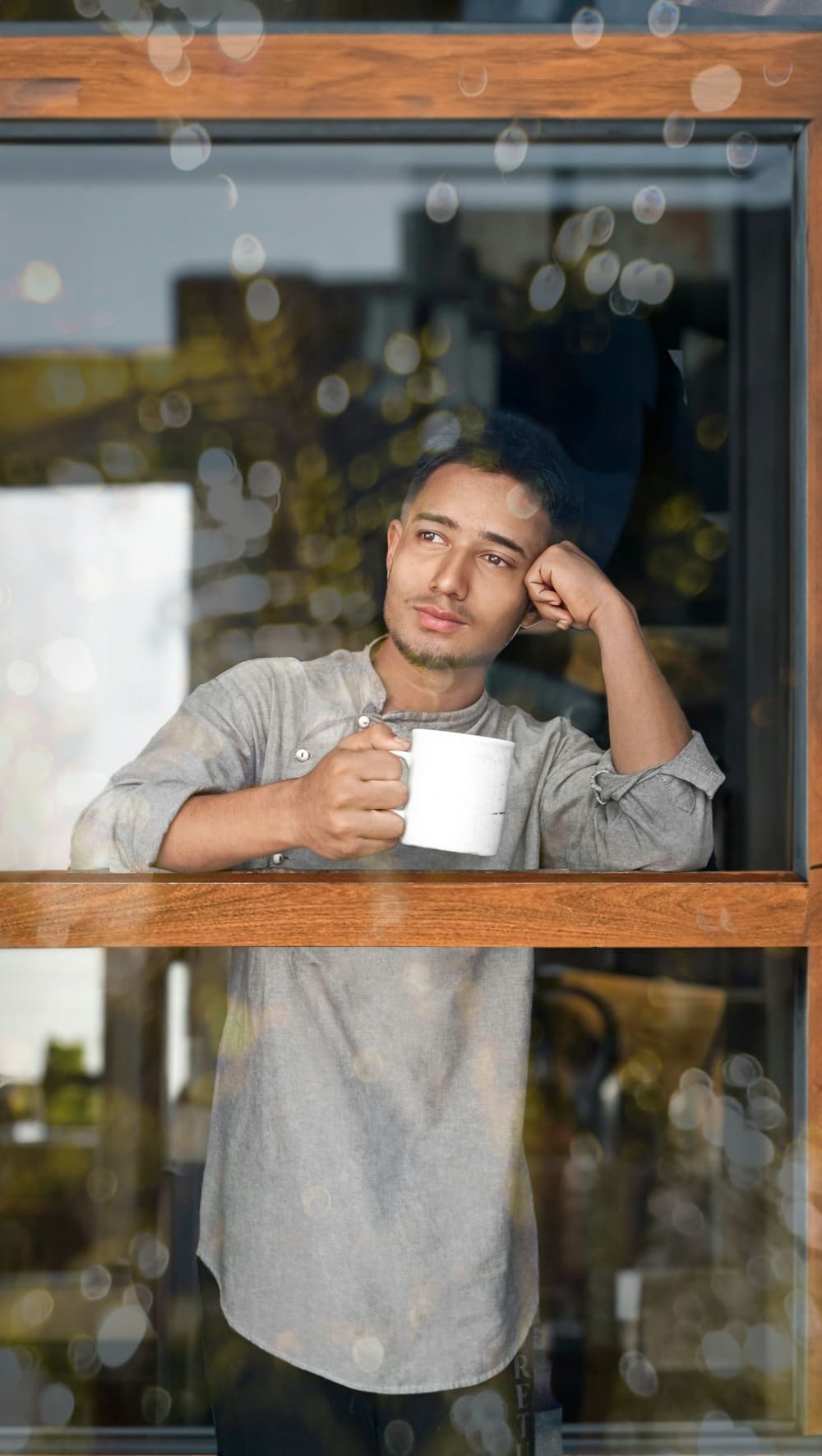 Un homme, un café à la main, réfléchit à la fenêtre de son appartement